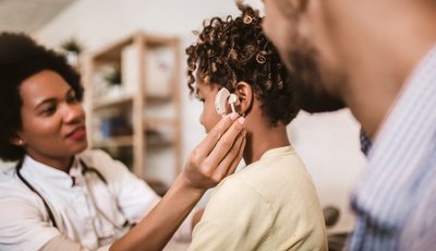 técnica en audiología protésica interactúa con uno niño y su padre